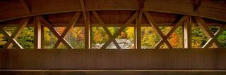 The interior Paddleford truss of the Albany Covered Bridge framing autumn foliage and the Swift River, White Mountains, New Hampshire.