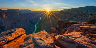 ine art landscape photograph of a dramatic starburst sunset over the Grand Canyon with the Colorado River visible far below, viewed from Toroweap Point.