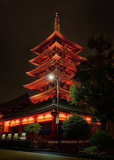 Illuminated multi-tiered temple at night in Tokyo, glowing red against dark sky, framed by trees and quiet courtyard.