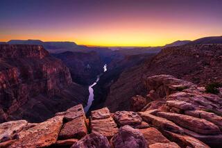 The Colorado River three thousand feet directly below the rim at Toroweap Overlook, with layered canyon walls under a purple and gold dusk sky, Grand Canyon.