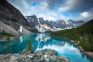 The serene turquoise lake, nestled amidst towering snow-capped mountains and verdant forests, offers a tranquil sanctuary for reflection and awe.