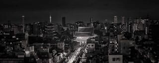 Black and white cityscape with a glowing path leading through urban streets toward a temple, blending modern buildings and history at night