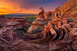 Swirling cross-bedded sandstone formations and a weathered hoodoo under an orange sunset sky, Coyote Buttes South, Vermilion Cliffs, Arizona