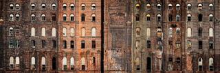 Weathered brick facade of the former Domino Sugar Refinery in Williamsburg, Brooklyn, with rows of arched windows, many boarded or broken.