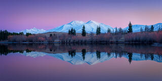 Still alpine lake reflecting snow covered mountains as early morning alpenglow colors the sky and peaks in Ashburton Lakes, New Zealand.