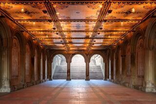 Symmetrical view of Bethesda Terrace in Central Park, New York City, with warm golden ceiling tiles, repeating stone arches, soft diffused light