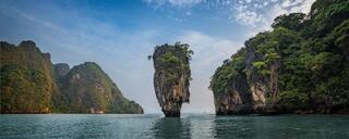 Ko Tapu, a narrow limestone sea stack, standing in open water between forested karst islands, Phang Nga Bay, Thailand.
