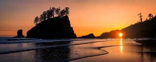 Golden sunset shining through a natural sea arch along the Washington coastline, with silhouetted rock formations and warm light reflecting across wet sand.