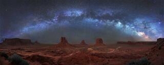 The Milky Way arching over the sandstone buttes and valley floor of Monument Valley at night, Navajo Nation, Arizona.