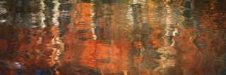 Abstract reflection of autumn leaves shimmering across a gently rippling stream, with warm reds, oranges, and golds blending into soft, flowing patterns water