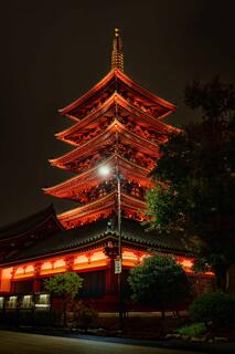 Illuminated multi-tiered temple at night in Tokyo, glowing red against dark sky, framed by trees and quiet courtyard.
