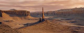 A tall sandstone spire standing above eroded badlands with mesas beyond, in warm evening light, Caineville Badlands, Utah.