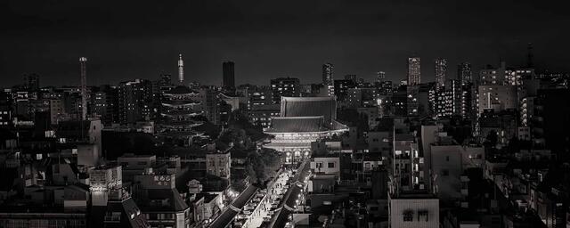 Black and white cityscape with a glowing path leading through urban streets toward a temple, blending modern buildings and history at night