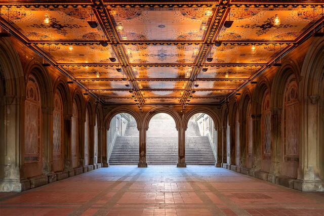 Symmetrical view of Bethesda Terrace in Central Park, New York City, with warm golden ceiling tiles, repeating stone arches, soft diffused light