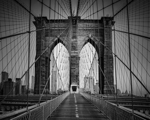 The Brooklyn Bridge walkway and its neo-Gothic stone tower with suspension cables, in black and white, New York City