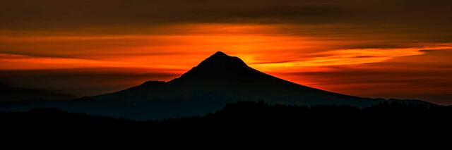 Mount Hood in full silhouette against an orange and red sunrise sky with forested ridges below, Oregon.