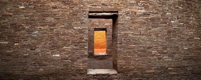 Ancient stone doorways aligned in a series of ruins in Arizona, with warm light illuminating the interior walls and passageways.
