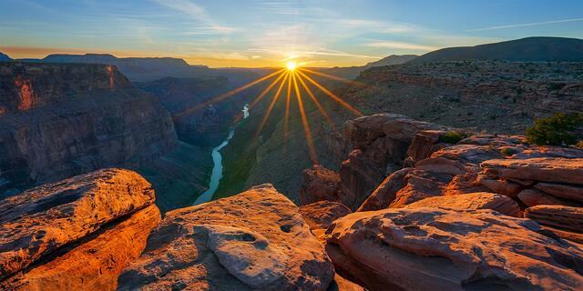 The sun at the horizon over the Colorado River in the inner gorge, with sunlit sandstone along the rim, Toroweap Overlook, Grand Canyon National Park.