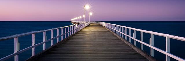 Urangan Pier at dusk, a long timber pier with white railings and lit lamp standards extending over the water at Hervey Bay, Queensland.