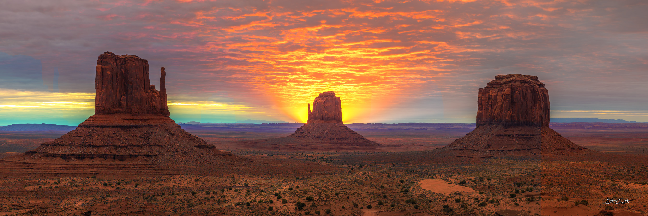 Golden Horizon The image depicts three prominent rock spires in the vast desert, set against a dramatic sky filled with hues of orange, pink, and purple as the sun rises on th