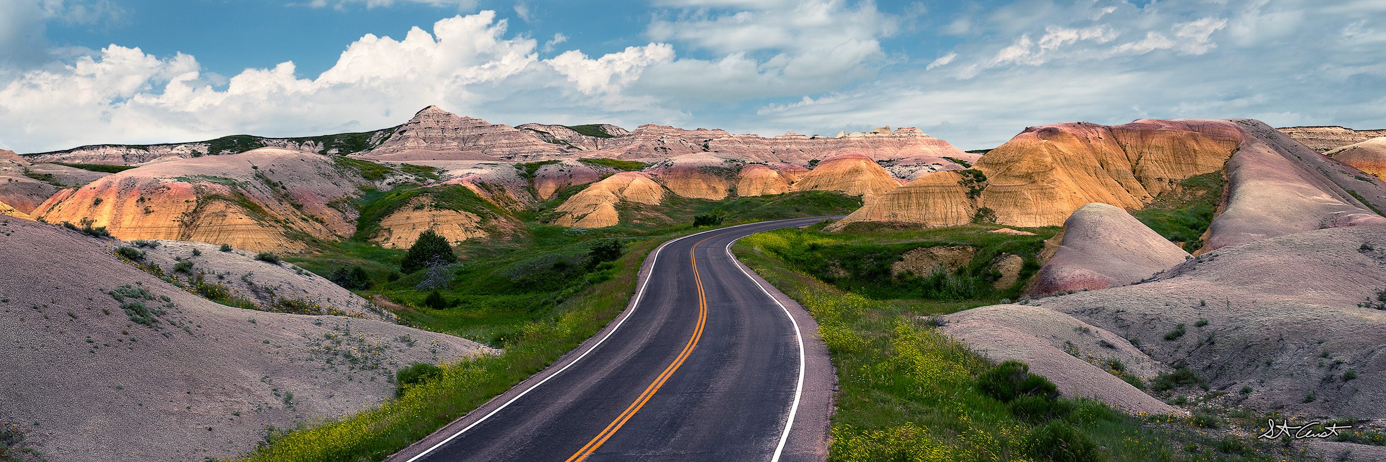 Terracotta Trails A serpentine road meanders through vibrant, multicolored badlands under a vast sky dotted with fluffy clouds.
