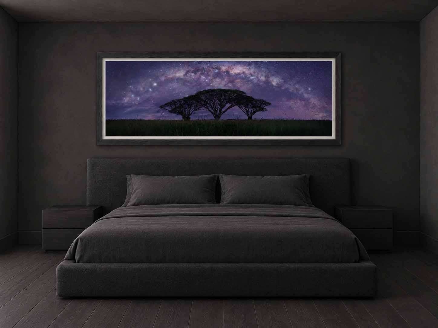 The Milky Way arching above three silhouetted trees near Rockhampton, Australia, framed in black with a white linen liner above a bed in a dark bedroom