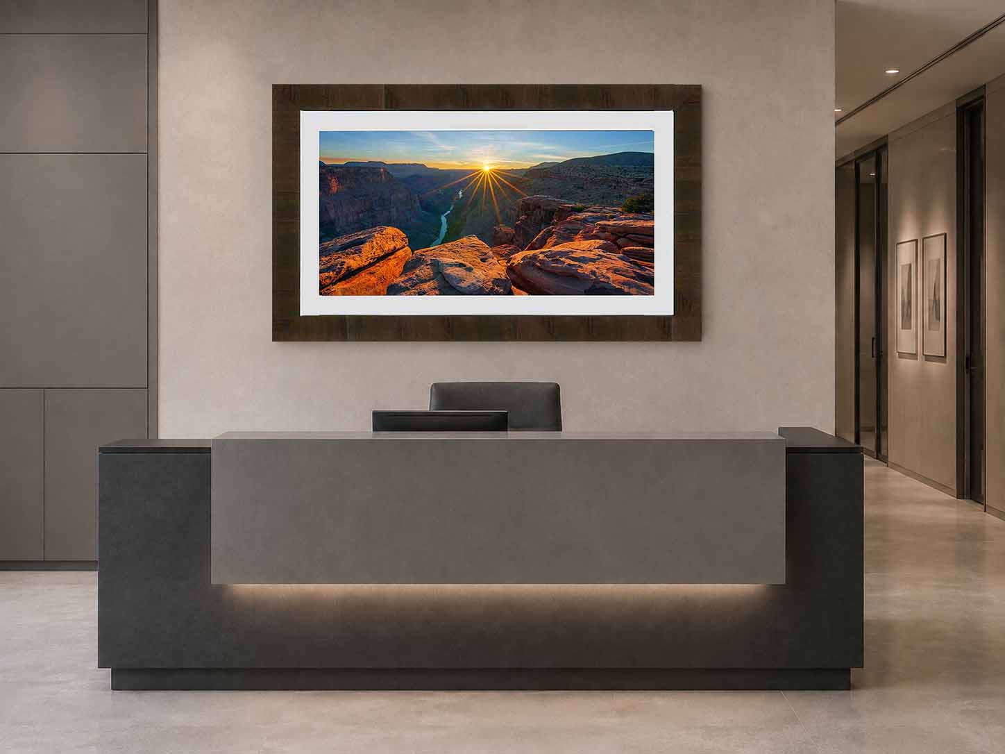 A photograph of sunset over the Colorado River at Toroweap, framed in dark ash with a white linen liner, above a stone reception desk in a corporate lobby.