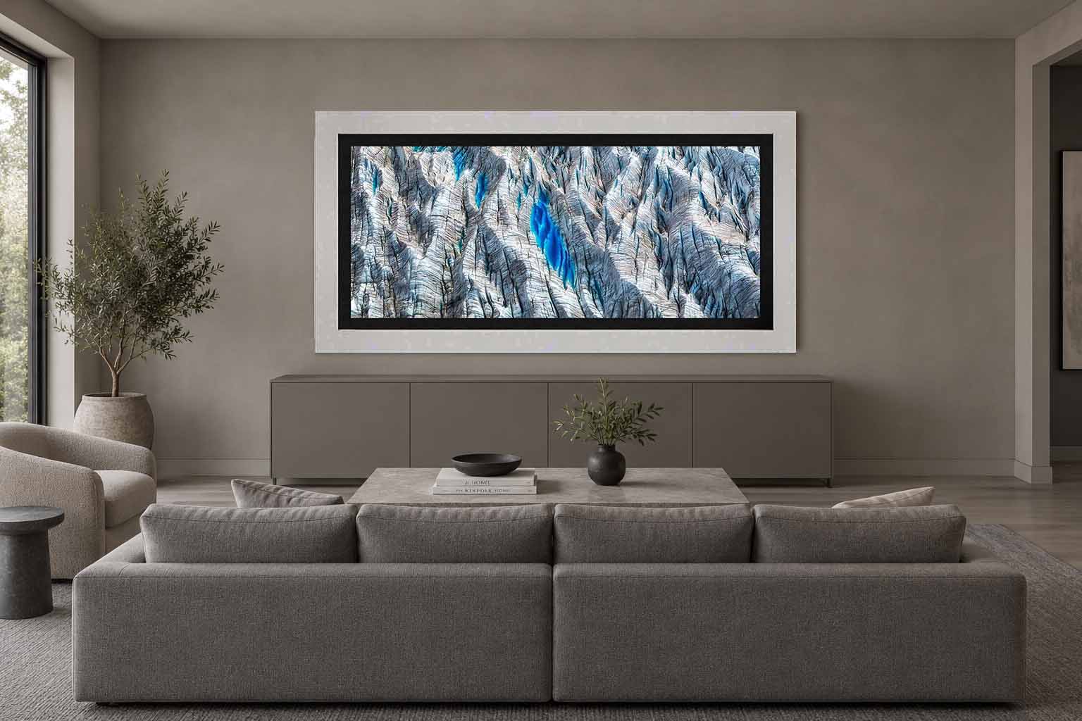 Meltwater pools in a crevassed Alaskan glacier seen from the air, framed in white with a black liner above a credenza in a gray living room