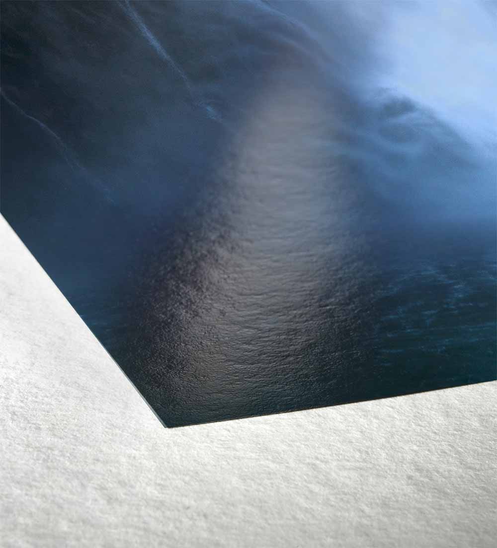 Close detail of a FineArt Baryta print corner lifted from the sheet, showing the gloss of the printed surface against the felt texture of the paper.