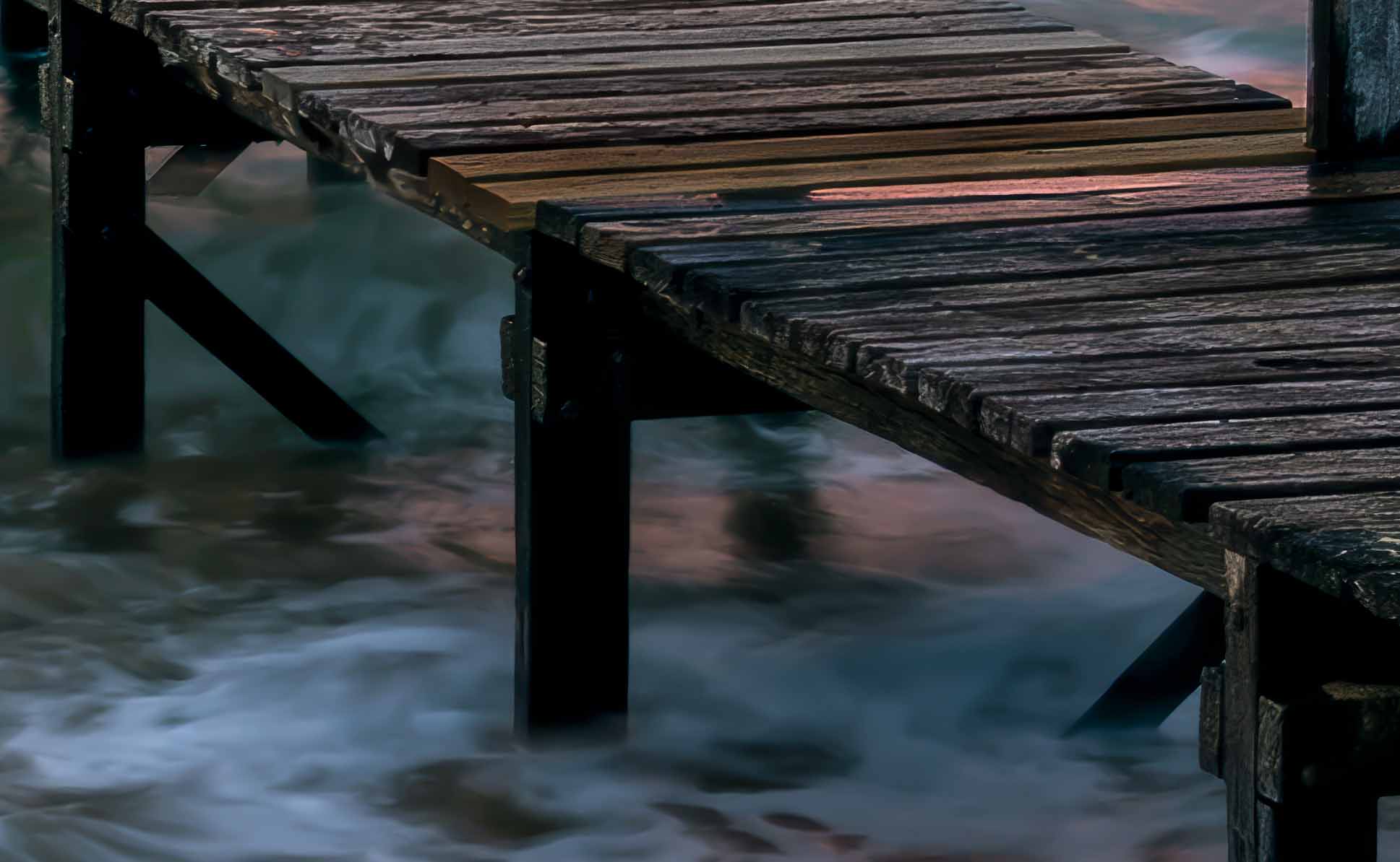 Detail of the weathered jetty planking at full resolution, with the surf rendered as continuous streaks by a long exposure.