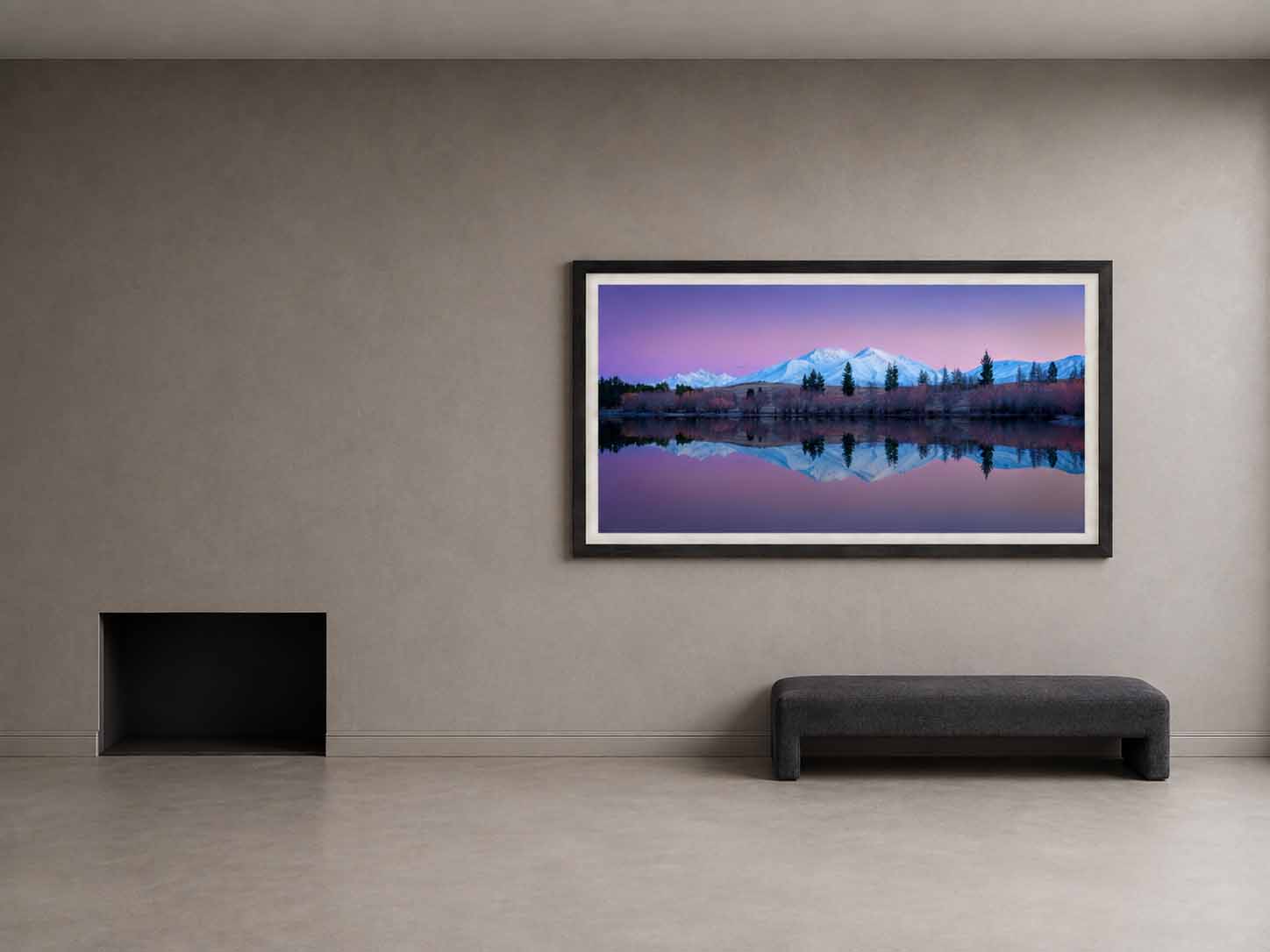 Snow-covered mountains mirrored in the still water of Lake Camp, Canterbury, framed in matte black with a white linen liner on a plaster wall in a quiet den.
