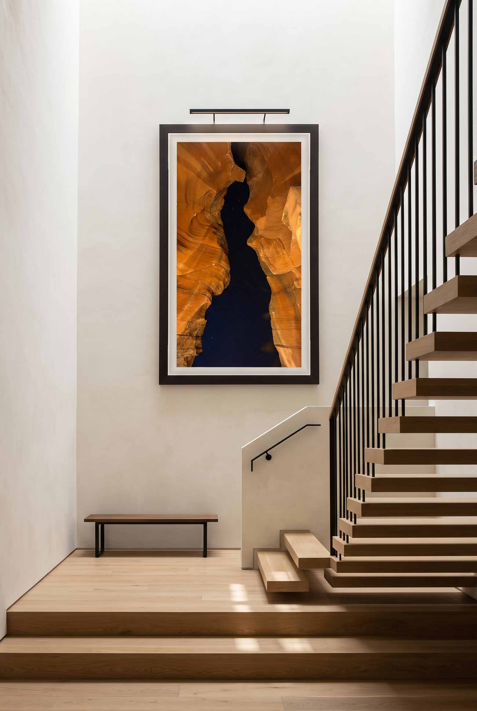 Lady in the Night displayed on a tall plaster wall above an open tread staircase, framed in Moda Satin Black with a white linen liner