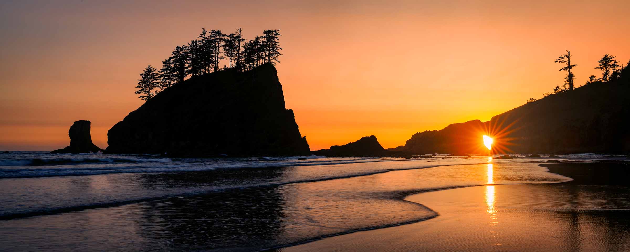 Last Glow Golden sunset shining through a natural sea arch along the Washington coastline, with silhouetted rock formations, with warm light reflecting across wet sand