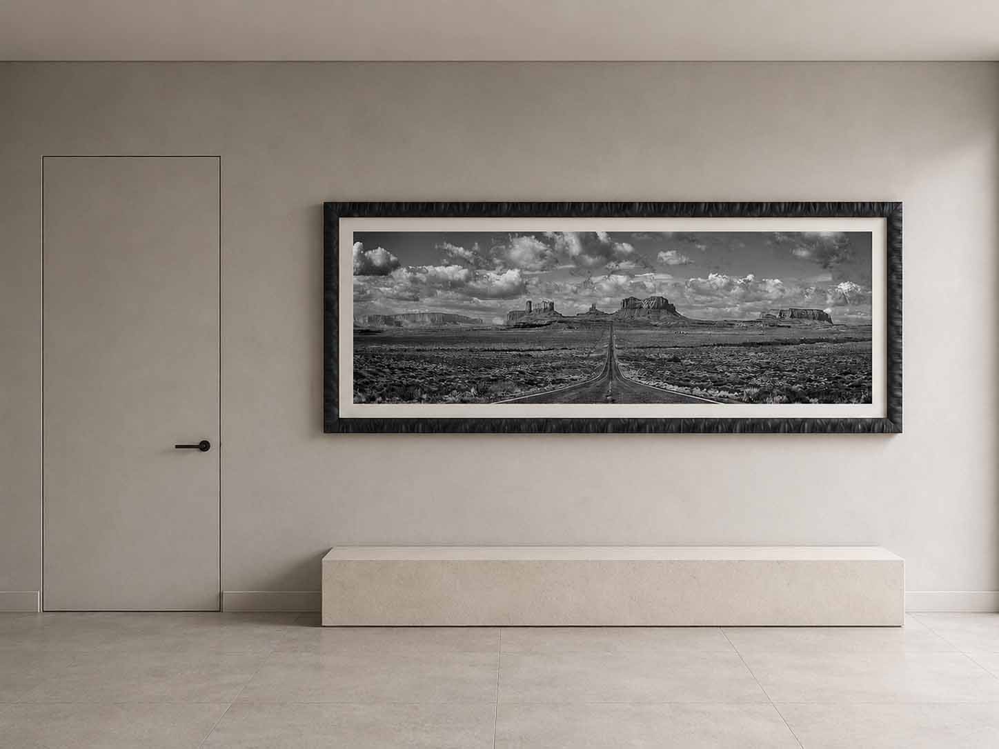 US 163 running toward the buttes of Monument Valley in black and white, framed in near-black with a white linen liner above a limestone bench in a quiet entry hall.