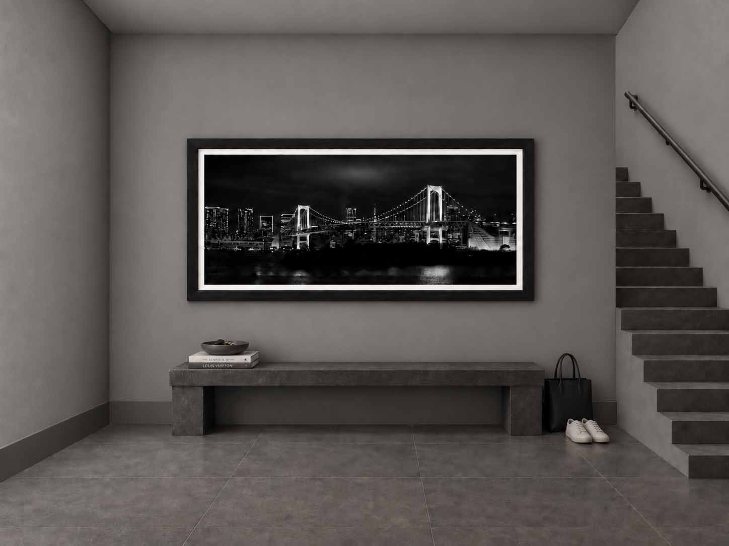 The Rainbow Bridge and Tokyo skyline at night in black and white, framed in satin black with a white linen liner above a stone bench in a gray entry