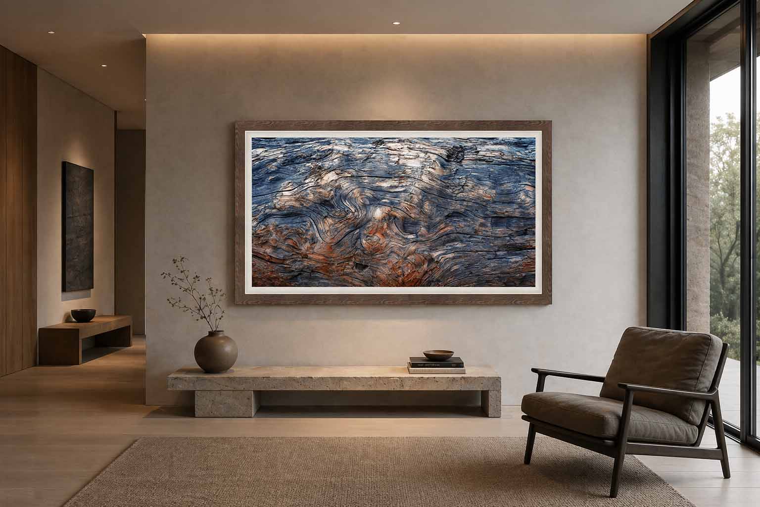Weathered driftwood grain from the beach at Bandon, Oregon, framed in warm gray-brown wood with a white linen liner above a stone bench in a quiet living room.