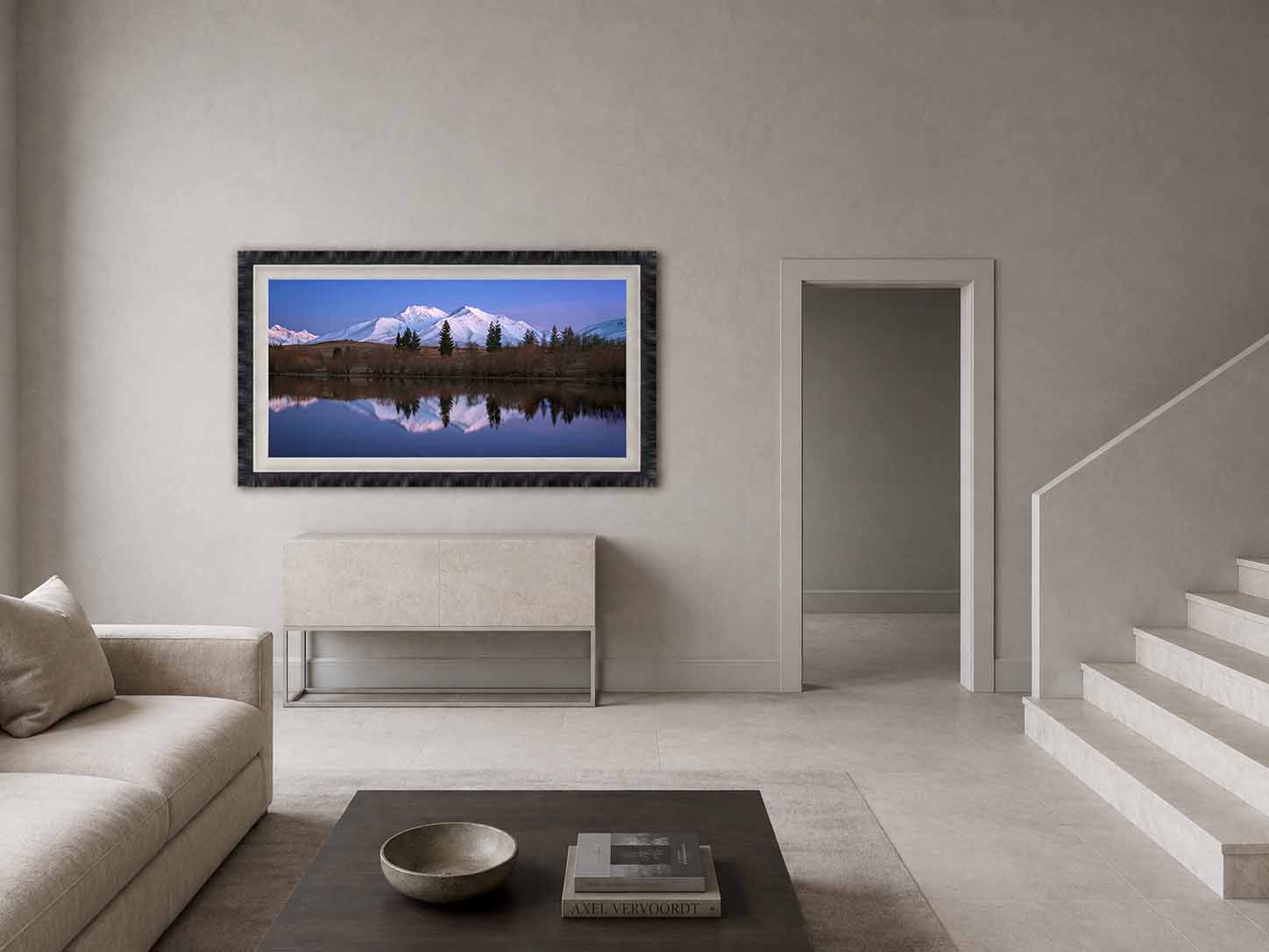 Snow-covered peaks of Mahaanui reflected in the still water of Lake Camp, Canterbury, framed in near-black with a white linen liner in a quiet great room.