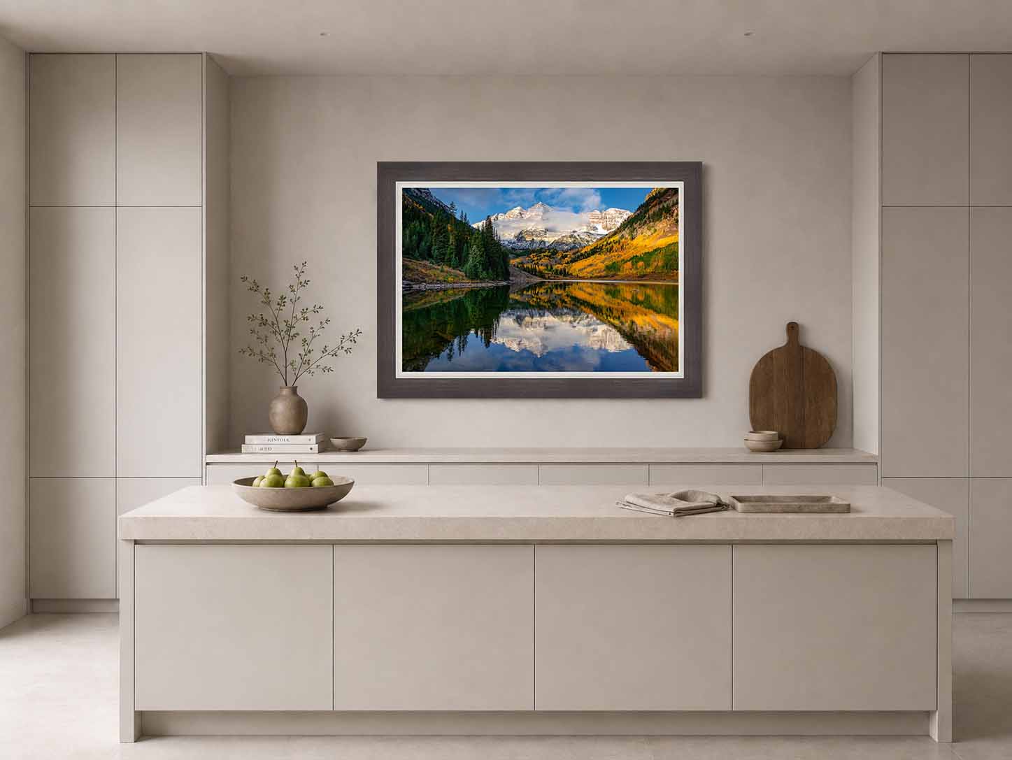 The Maroon Bells reflected in Maroon Lake with autumn aspen, framed in dark wood with a white liner above a pale island in a quiet kitchen.