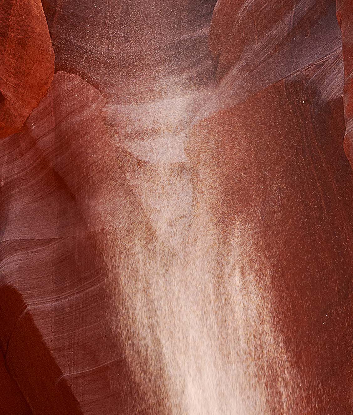 Detail at full resolution showing the figure formed in the falling sand, with a rounded head shape and a dark horizontal band beneath it reading as shoulders.
