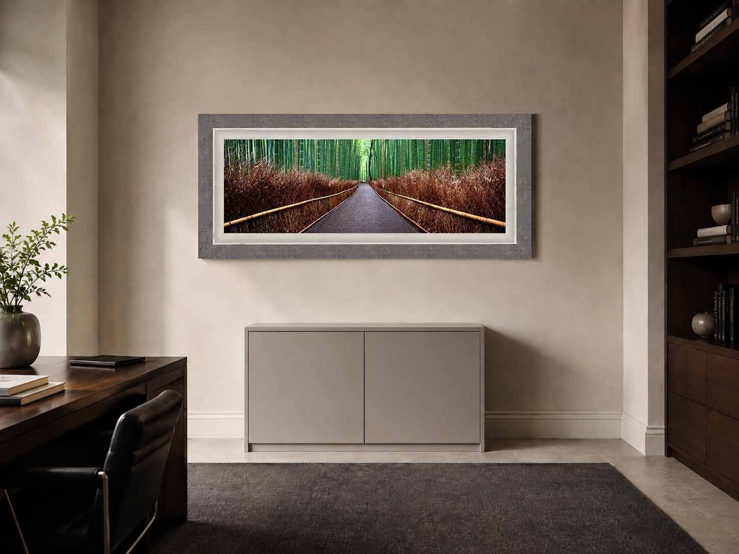 A panoramic photograph of the bamboo grove path at Arashiyama, framed in gray shagreen with a white linen liner, above a pale cabinet in a study.