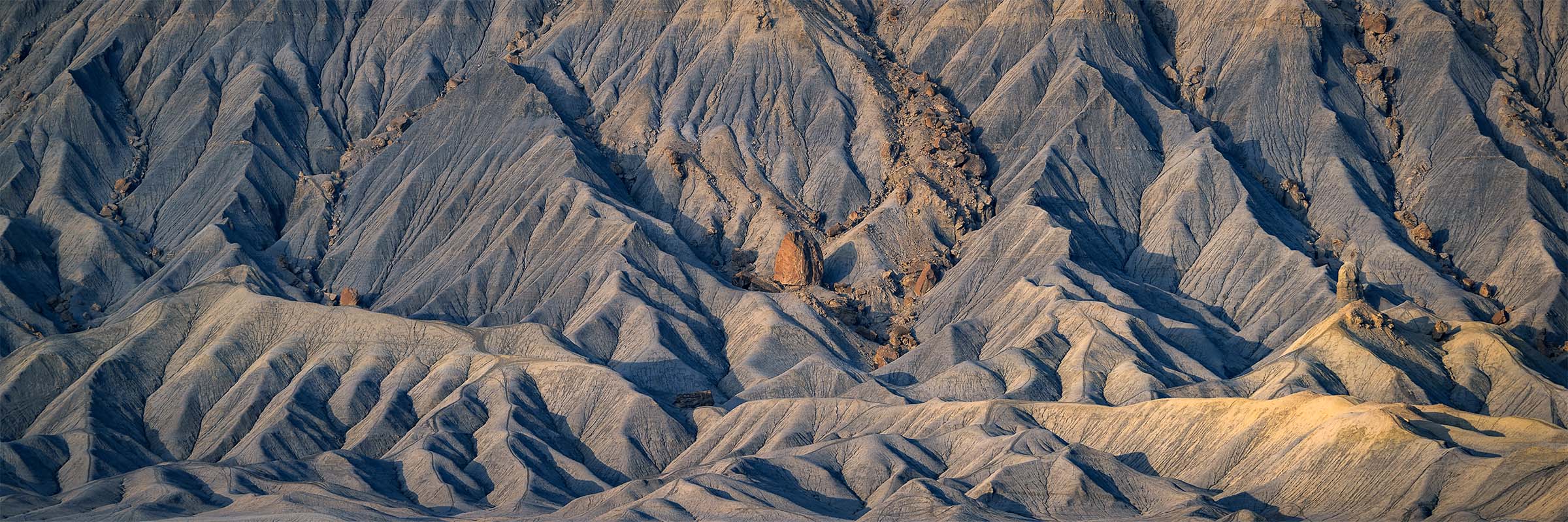 Layered sandstone ridges in Utah illuminated by soft morning light, revealing erosion patterns and a solitary rock formation.