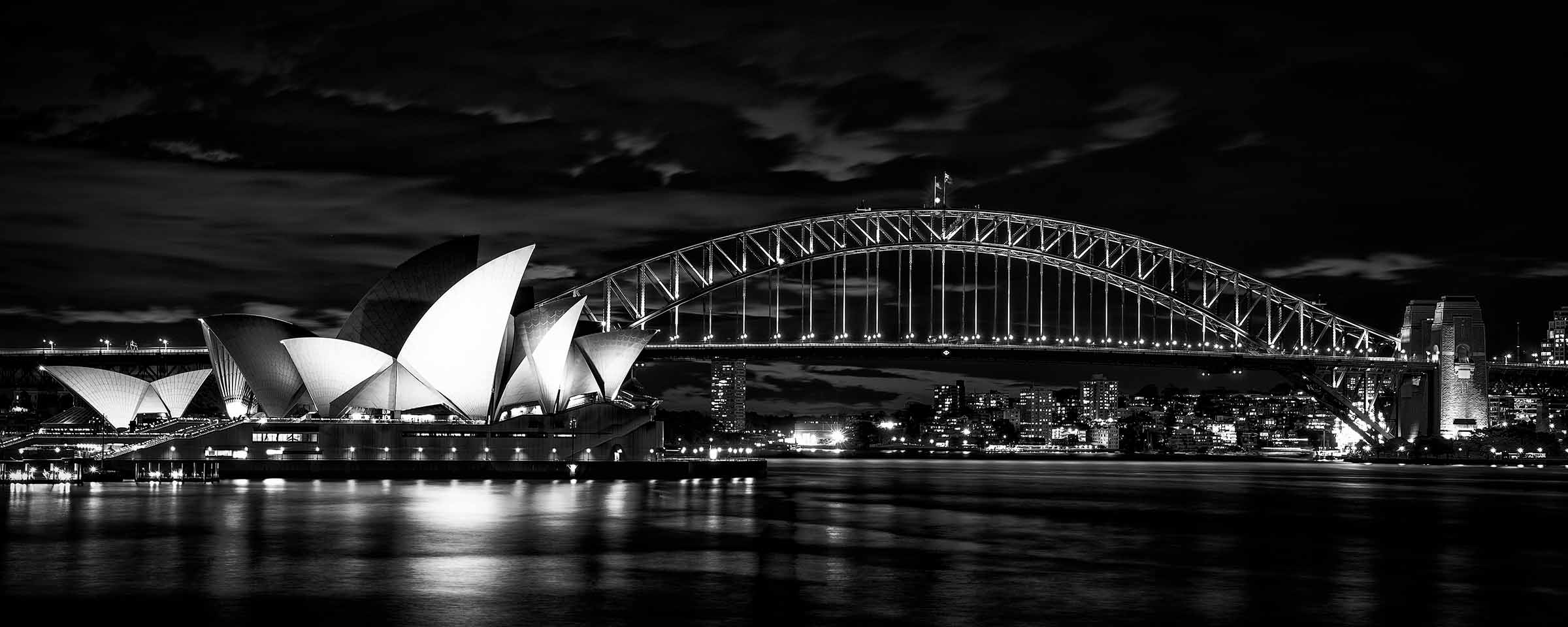 Nightfall at the Opera Black and white photograph of the Sydney Opera House and Harbour Bridge at night, illuminated against a dark sky, with city lights reflecting across the water