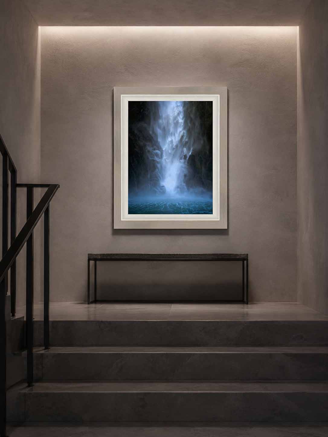 The Apparition shown as a framed print above a steel bench at a stair landing in a plaster and stone stairwell, in a Ramino Night Silver moulding with a white linen liner