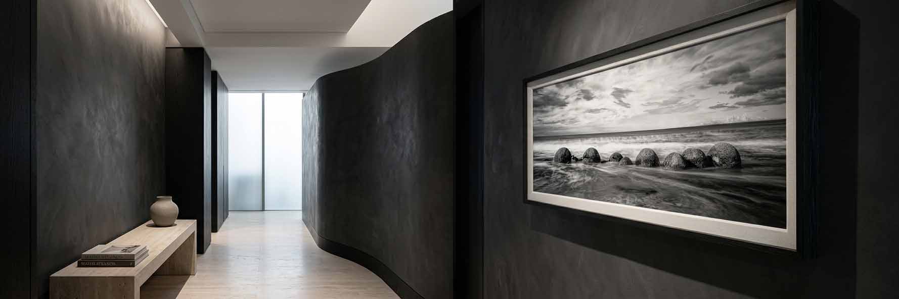 The Gathering shown as a framed black and white print on a dark plaster wall in a hallway, in a black moulding with a white linen liner