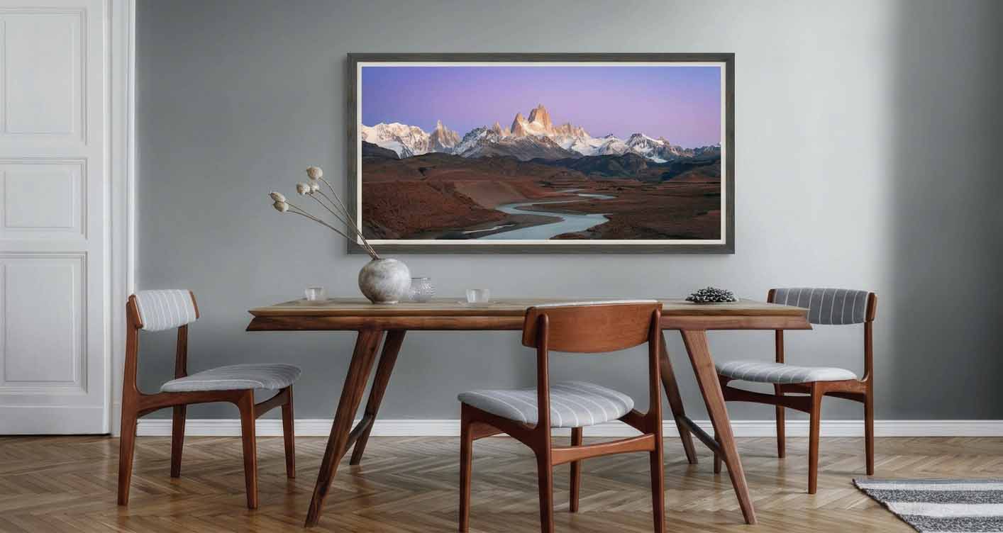 Monte Fitz Roy at sunrise above the Patagonian steppe, framed in gray with a white liner above a walnut table in a quiet dining room.