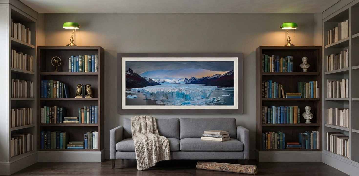The calving face of the Perito Moreno Glacier under a breaking sky, framed in gray-brown with a white liner above a charcoal bench in a quiet library.