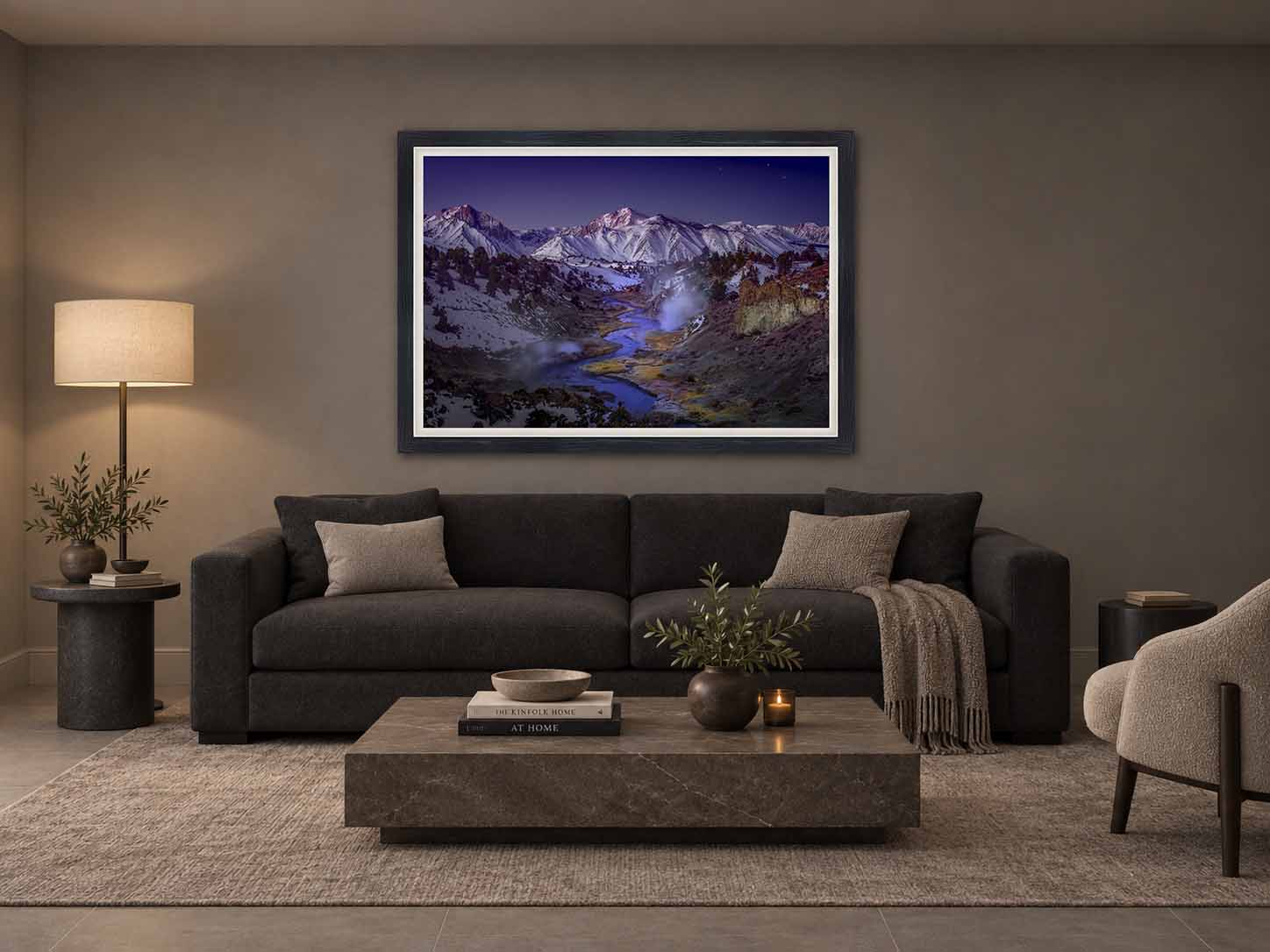 Steam rising from Hot Creek before dawn beneath the snow-covered Sierra Nevada, framed in dark wood with a white liner above a charcoal sofa in a dim family room.